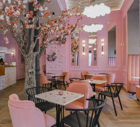 Kuva kahvilan sisältä, kuvassa kahvilan pöydät, vaaleanpuanist seinät ja kirsikkapuu kukassa